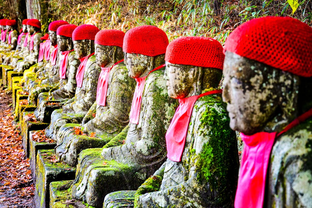 Moss-covered Buddha statues with red caps in Nikko Japan