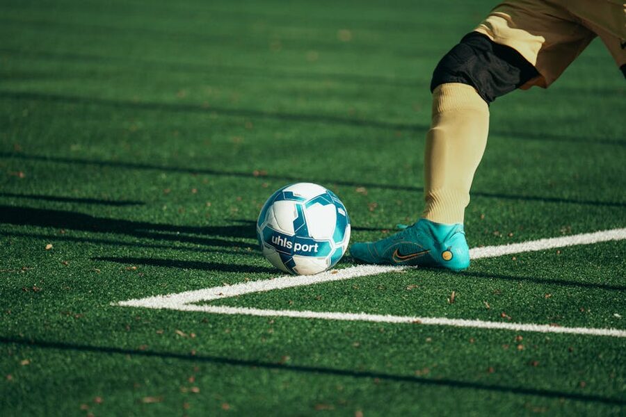 Football boot resting on a ball on green grass pitch